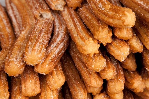 Foto colorida de churros, dispostos um em cima do outro e com açúcar polvilhado - Metrópoles