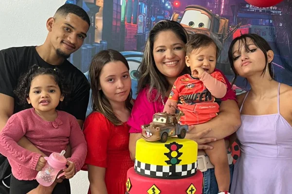 foto colorida de família reunida atrás da mesa do bolo em festa de aniversário. Na foto, um homem e uma mulher ao lado de 4 crianças.