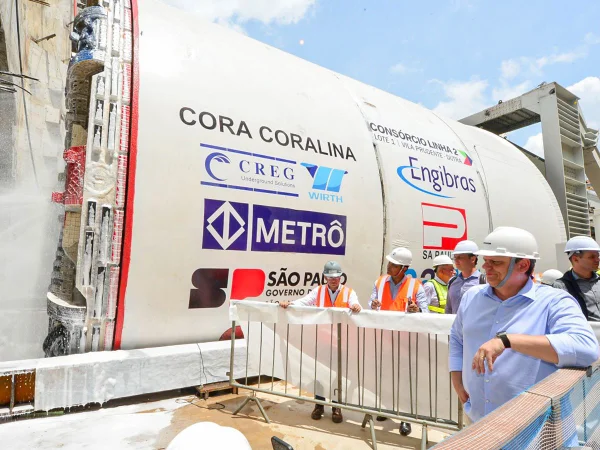 Imagem colorida mostra Tarcísio de Freitas, à direita, apoiando o braço em uma grade, vendo uma máquina tuneladora de Metrô - Metrópoles