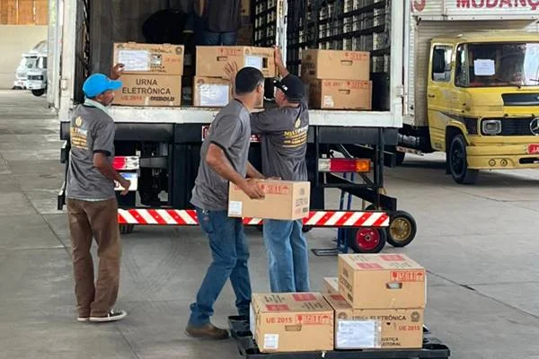 Fotografia colorida de urnas sendo colocadas em caminhão