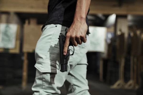 Porte e porte de arma. Homem usando calça caqui e camiseta preta segurando uma arma de fogo na cor preta em uma das mãos- Metrópoles