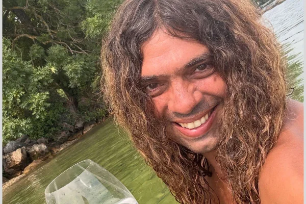 Imagens coloridas mostram homem jovem, cabelos longos, castanhos e ondulados, sorrindo e com uma taça na mão