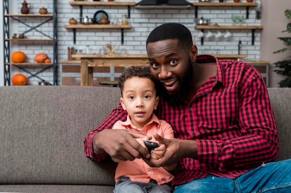 Homem negro e filho assistindo tv