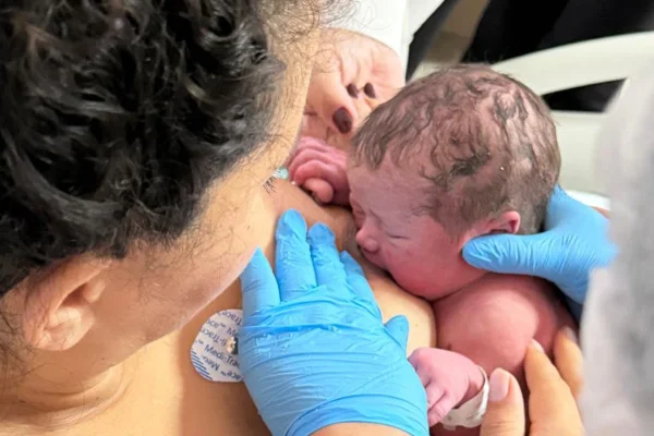 Foto colorida de mulher amamentando o bebê - Matéria Metrópoles.