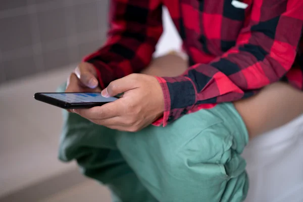 Homem usando um smartphone enquanto está sentado no vaso sanitário. Metrópoles