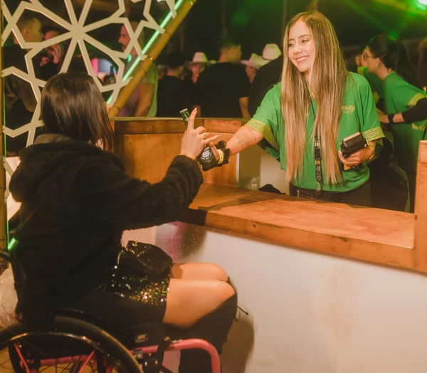 Fotografia colorida mostrando mulher entregando cerveja em bar para cadeirante-Metrópoles