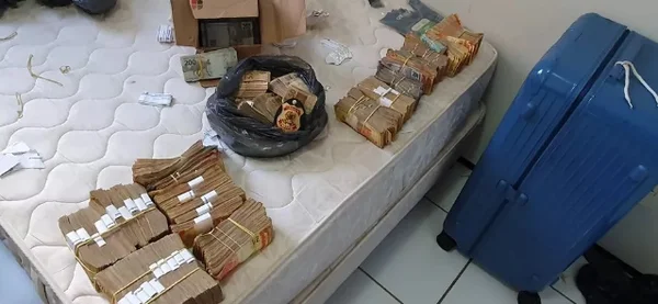 Dinheiro apreendido durante operação que apura fraudes na Codevasf, orgão sob o comando de entidades do chamado "centrão". Na foto, maços de dinheiro são agrupados sob colchão e mala azul aparece ao lado - Metrópoles