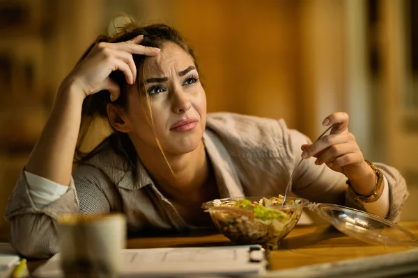 Foto colorida de mulher com expressão de culpa ao comer