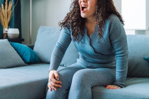 Imagem colorida: mulher com a mão no joelho grita de dor - Metrópoles
