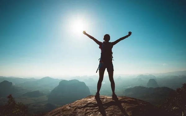 Uma pessoa em cima de uma pedra no topo de um morro com os braços abertos