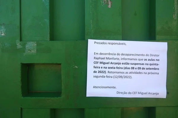 foto colorida de aviso em papel branco colado em portão verde