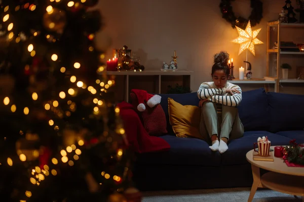 Imagem mostra mulher sentada no sofá com postura triste. Uma árvore de Natal está em primeiro plano - Metrópoles
