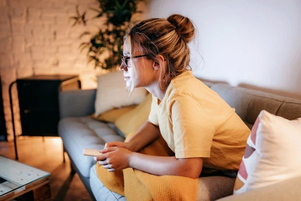 Foto mostra mulher jovem assistindo TV a noite - Metrópoles - hábitos noturnos