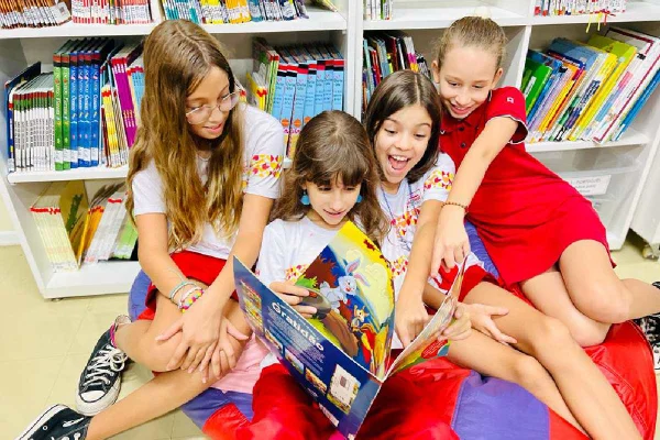 foto colorida de crianças olhando um livro- Metropoles