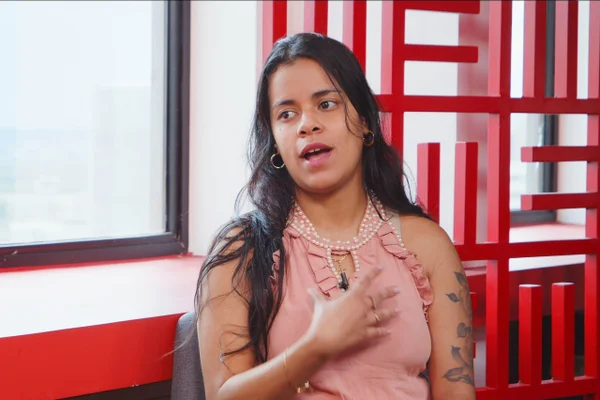 Mulher de cabelos pretos e camiseta rosa concede entrevista ao Metrópoles