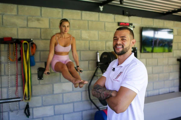 Homem com os braços cruzados ao fundo uma mulher se exercita