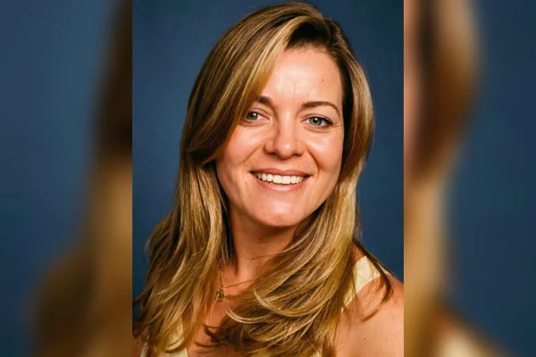 Foto colorida de mulher loira sorrindo para foto com fundo azul escuro - Metrópoles