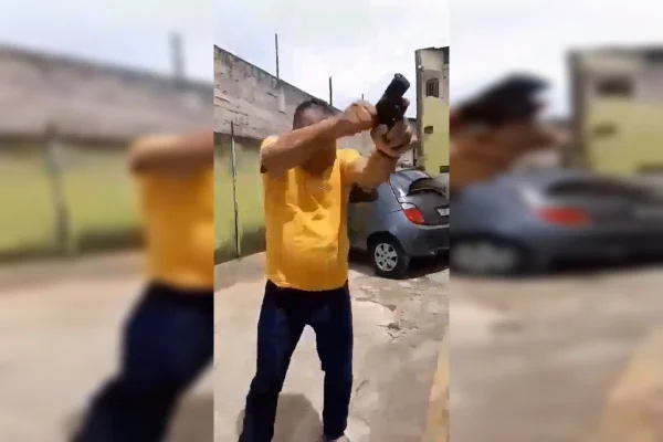 Imagem colorida. Homem de camisa amarela e calça jeans com arma na mão