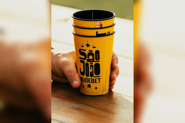 Uma mão segura um copo amarelo escrito São João Vai de Bet, da festa de São João da prefeitura de São Paulo