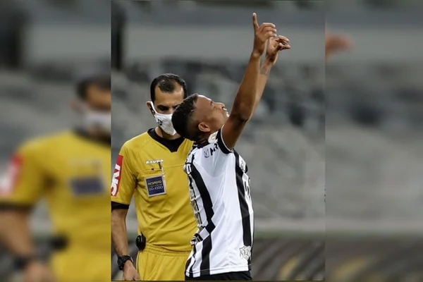 Keno com apontando para o céu e homem de amarelo ao fundo