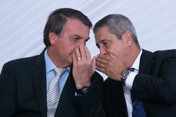 Imagem colorida de Bolsonaro e Braga Netto conversando cobrindo as bocas com as mãos