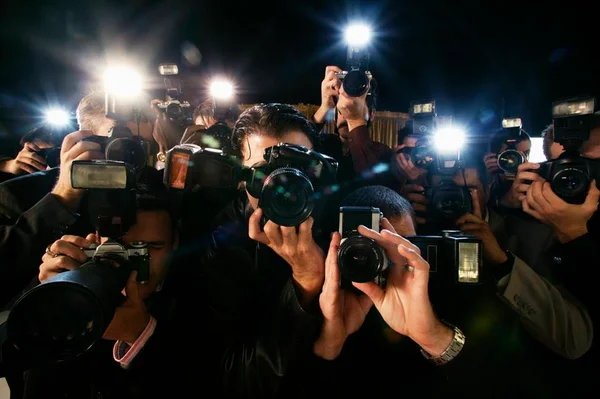 Foto colorida de vários paparazzi juntos com a câmera no rosto fotografando alguém - Metrópoles
