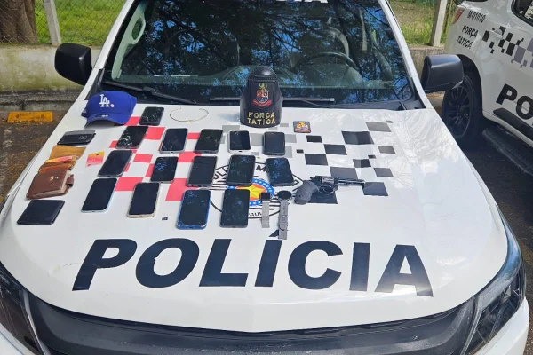 Imagem colorida de celulares em cima de capô de viatura policial. Metrópoles
