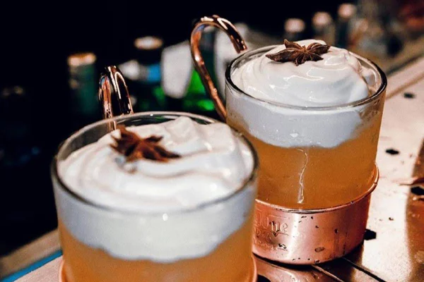 na foto temos dois copos com drinque amarelo e espuma