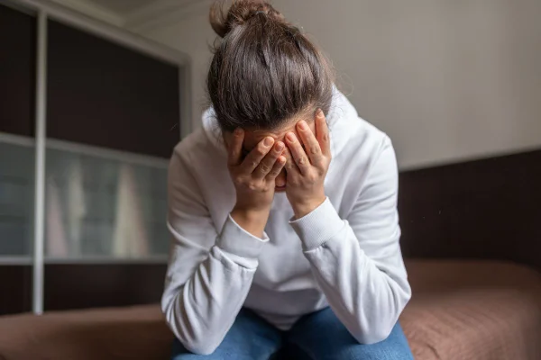 mulher de cabeça baixa com as mãos no rosto