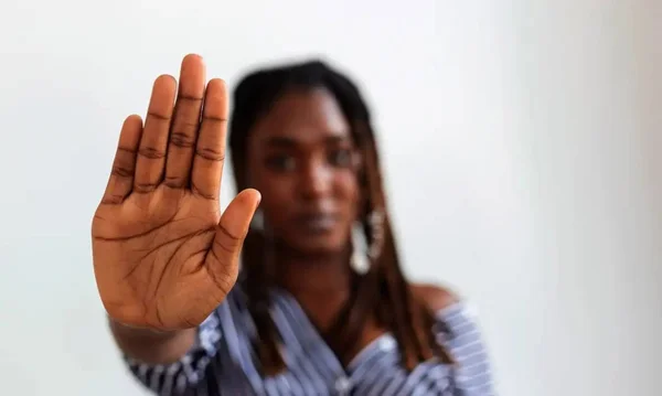 Imagem colorida de uma mulher negra com a palma da mão aberta em sinal de pare - Metrópoles