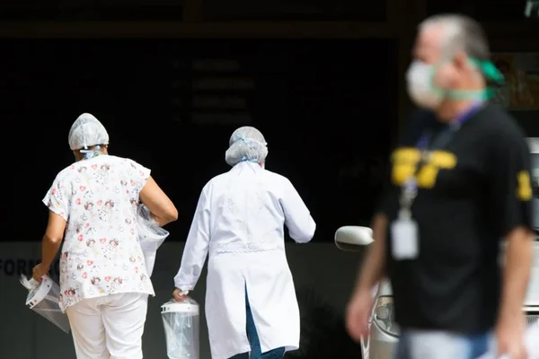 Dois servidores da Saúde vestidos de branco com um homem de preto