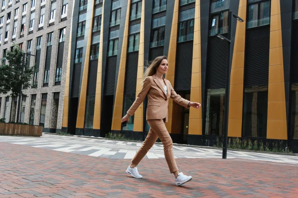 Jovem mulher caminhando em passo firme frente a um prédio na rua - Metrópoles