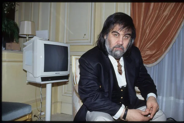 O compositor grego Vangelis, que compôs a conhecida trilha sonoro do filme "Carruagens de Fogo". Ele tem cabelo longo e escuro, barba e usa terno, sentado num quarto com móveis rebuscados - Metrópoles