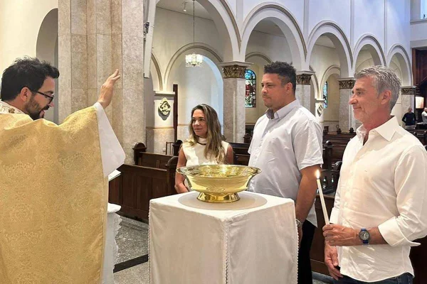 foto colorida de ronaldo fenômeno de camisa azul clara entre uma mulher e um homem e de frente para padre fabio de melo em igreja- metrópoles
