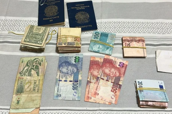 Imagem colorida de dinheiro e passaportes apreendidos em operação. Metrópoles