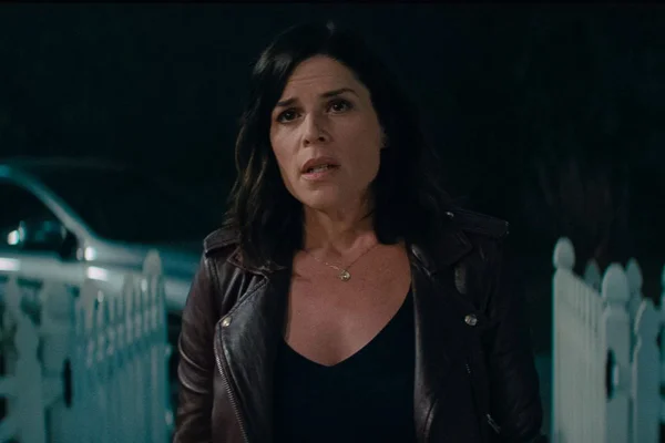 Neve Campbell em foto colorida. Ela é uma mulher branca, de cabelo preto na altura dos ombros. Usa jaqueta preta e uma blusa preta - Metrópoles