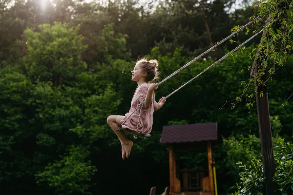 Imagem mostra menina pequena brincando no balanço em fundo de árvores - Metrópoles