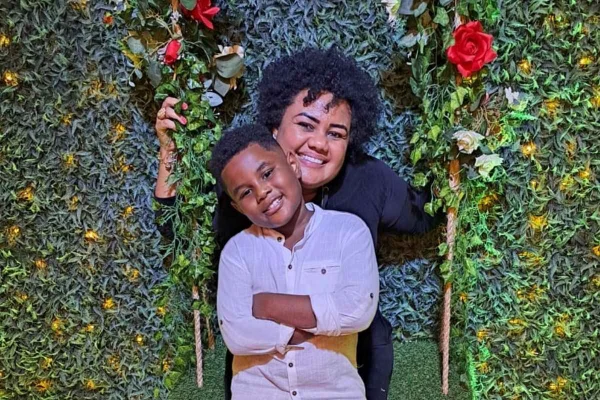 Imagem colorida de Nayara e do filho Arthur Antonio, que são negros e sorriem para a foto. Ele está na frente, com os braços cruzados, de camisa de botão branca. Ele está atrás, de camiseta preta - Metrópoles