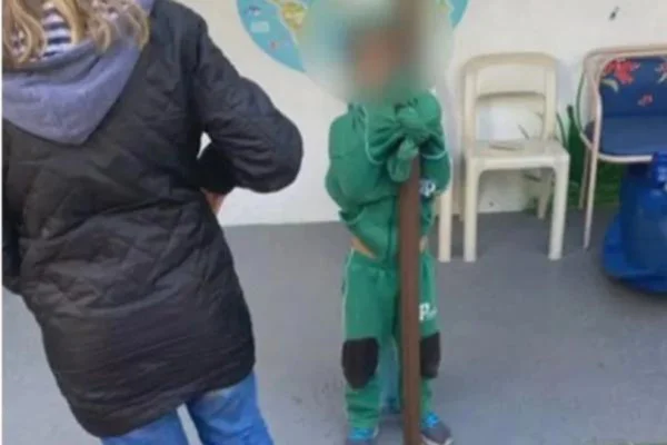 Imagem colorida de criança da Escola Pequiá. Ela aparece amarrada pela roupa a um poste - Metrópoles