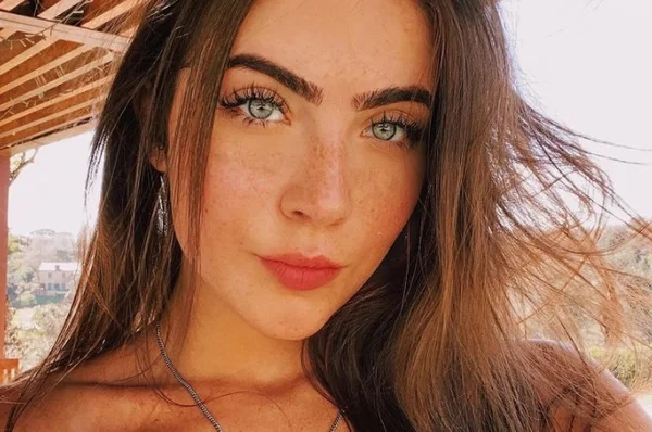 Menina branca de olho azul e cabelo preto tirando uma selfie mostrando o rosto com sardinhas