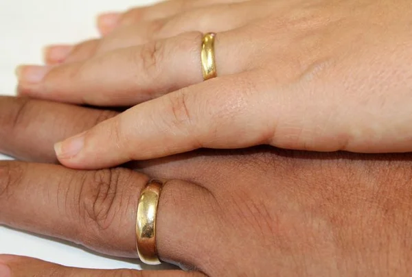 Fotografia colorida de casal posando com as mãos sobrepostas com aliança no dedo