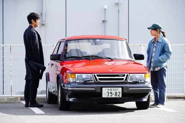 Homem e mulher em frente a um carro vermelho
