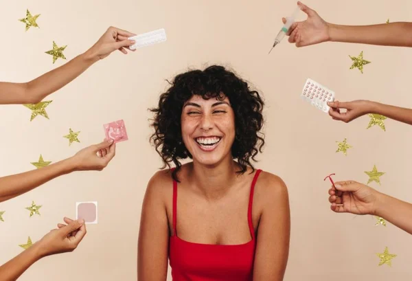 Mulher sorrindo e em volta dela vários métodos contraceptivos para o dia do orgasmo - Metrópoles