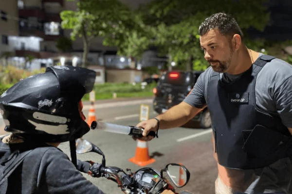 Imagem colorida de um motociclista sendo abordado e realizando o teste do bafômetro - Metrópoles