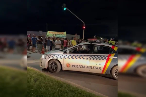 Imagem de moradores protestando em uma rodovia. À frente, há uma viatura da PMDF