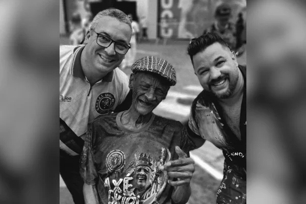 Imagem em preto e branco mostra Seu Carlão, fundador da escola de samba Unidos do Peruche, entre dois integrantes da escola - Metrópoes
