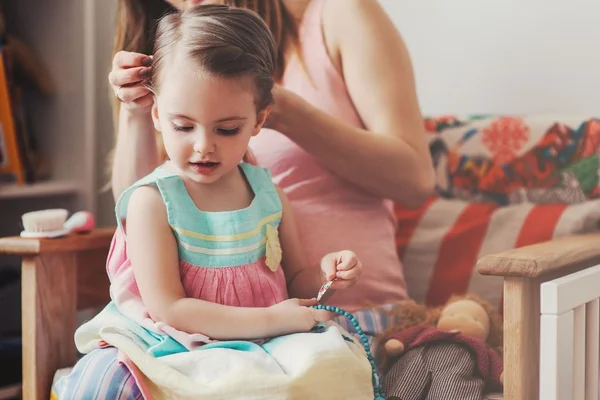 menina tendo o cabelo penteado pela mãe em foto colorida