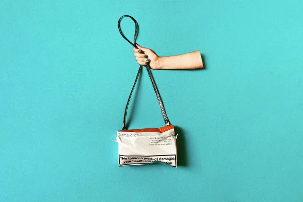 Arte feita estilo colagem pela artista britânica Martha Haversham. Na imagem aparece um braço branco, com uma mão que tem unhas pintadas de vermelho, segurando uma bolsa feita a partir de uma embalagem de uma bala. A artista faz peças com itens que seriam descartados ou restos de alimentos.