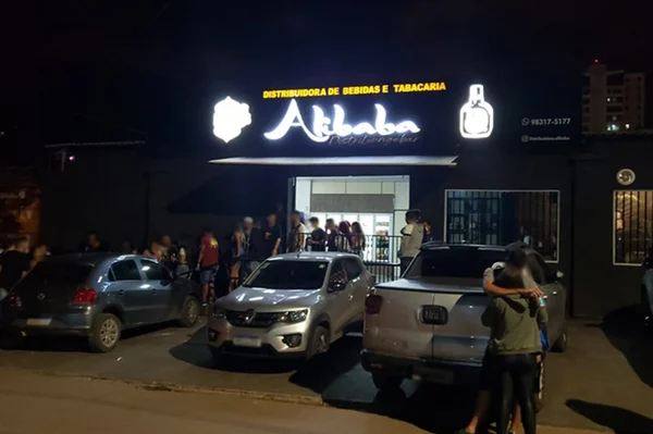 Fachada de bar com carros estacionados na frente e pessoas na saída