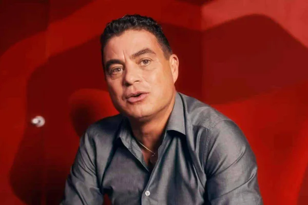 Dhomini vestindo cinza em frente a um fundo vermelho - Metrópoles